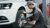 Osoba koja nosi zaštitnu opremu koristi udarni ključ za pričvršćivanje kotača automobila.