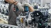 Osoba koja nosi zaštitnu opremu koristi bežični udarni ključ na sklopu motora.