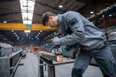 Radnik u zaštitnoj opremi brusi metal u industrijskoj radionici.