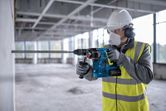 Osoba u zaštitnoj opremi buši beton bežičnim rotacijskim čekićem.