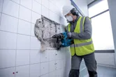 Osoba koja nosi zaštitnu opremu koristi bežični rotacijski čekić za probijanje popločanog zida.