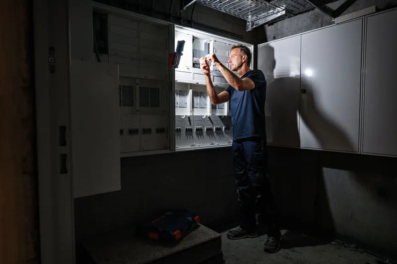 Osoba koja nosi zaštitnu opremu popravlja električnu ploču pod jakim svjetlom.