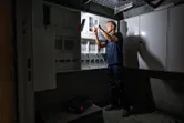 Osoba koja nosi zaštitnu opremu popravlja električnu ploču pod jakim svjetlom.