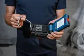 Osoba drži kompaktnu LED radnu svjetiljku s priloženom baterijom u industrijskom okruženju.