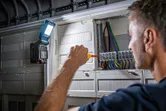 Osoba radi na električnoj ploči sa svjetiljkom koja osvjetljava ožičenje.