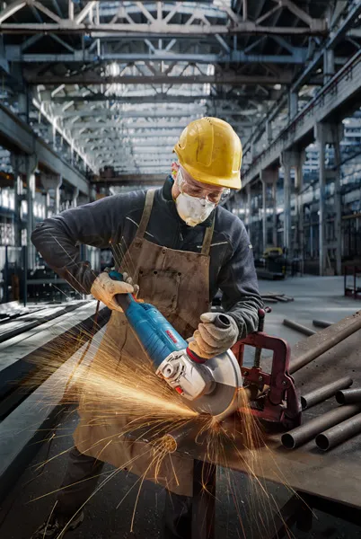Osoba koja nosi zaštitnu opremu brusi metalne cijevi na radnom stolu u tvornici.