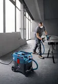 Osoba koja nosi zaštitnu opremu reže materijal pilom spojenom na višenamjenski usisavač.