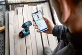 Osoba provjerava značajke aplikacije električnog alata na pametnom telefonu u blizini bežične bušilice.