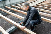 Osoba u zaštitnoj opremi pričvršćuje drvene grede električnom bušilicom na gradilištu.