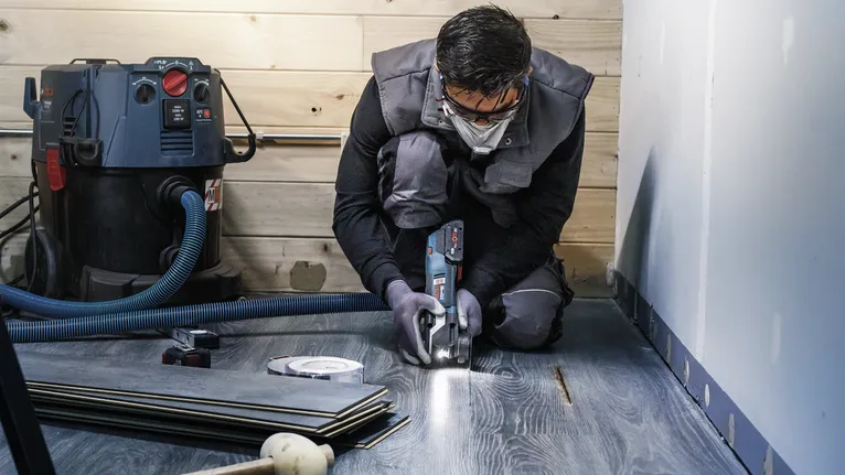 Osoba u zaštitnoj opremi reže laminatni pod električnim alatom.