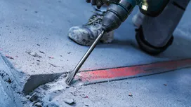 Osoba koja nosi zaštitnu opremu koristi električni alat za razbijanje betona.