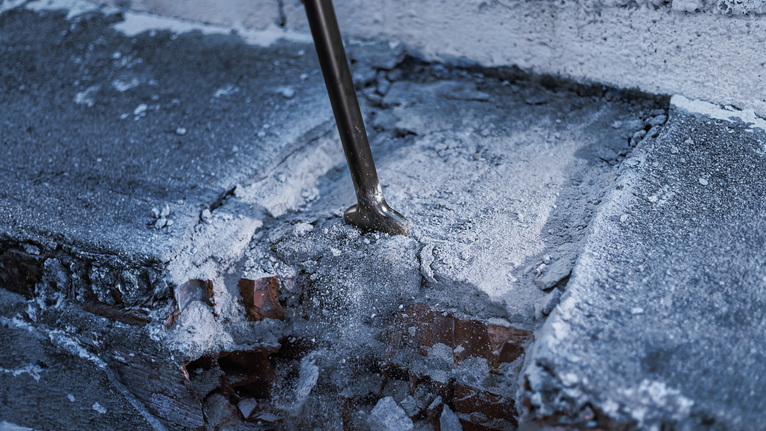 Dlijeto probija betonsku površinu s raspršenom prašinom i krhotinama.