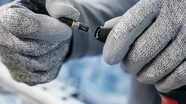 Osoba koja nosi zaštitnu opremu drži odvijač blizu nastavka za bušilicu.