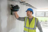 Osoba u zaštitnoj opremi poravnava laserski nivelman na nedovršenom zidu.
