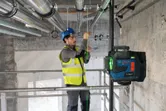 Osoba koja nosi zaštitnu opremu poravnava cijev pomoću laserskog nivelatora.