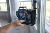 Osoba drži laserski nivelator uz metalni okvir na gradilištu.