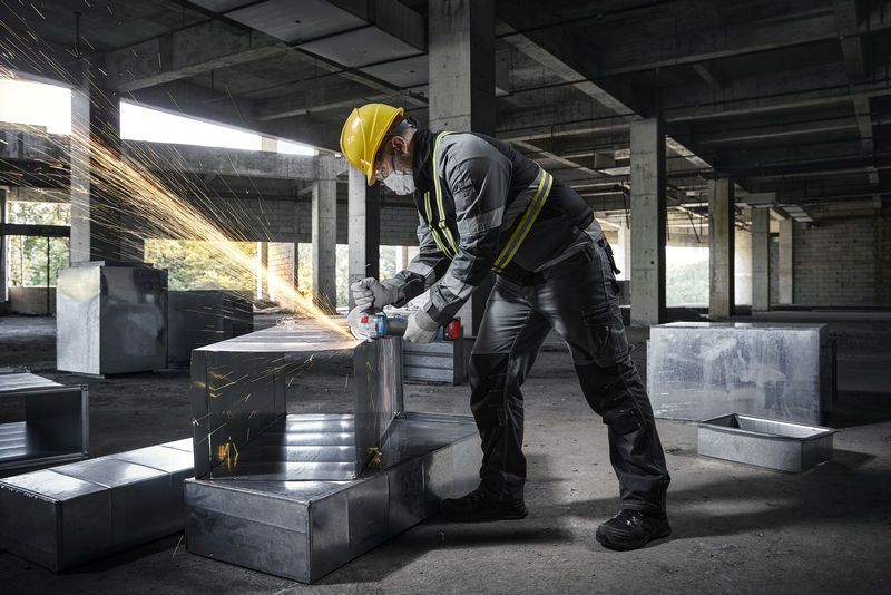 Osoba koja nosi zaštitnu opremu koristi kutnu brusilicu na metalnom kanalu na gradilištu.