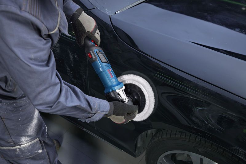 Osoba koja nosi zaštitnu opremu polira vrata automobila pomoću električne polirke.