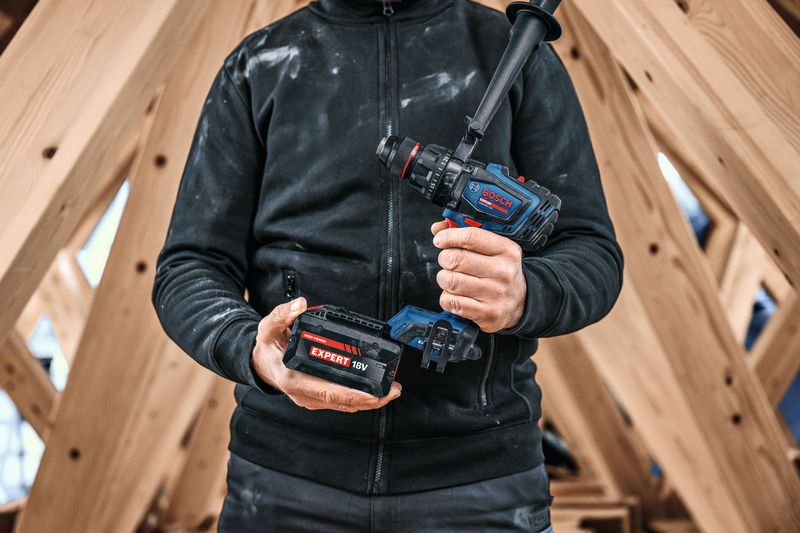 Osoba koja nosi zaštitnu opremu drži bežičnu kombiniranu bušilicu i baterijski paket.