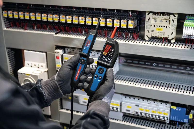 Osoba koja nosi zaštitnu opremu koristi tester napona na električnoj ploči.