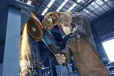 Osoba koja nosi zaštitnu opremu brusi metal, stvarajući iskre u industrijskoj radionici.