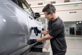 Osoba koja nosi zaštitnu opremu brusi vrata automobila pomoću brusilice s ekscentričnom orbitom.