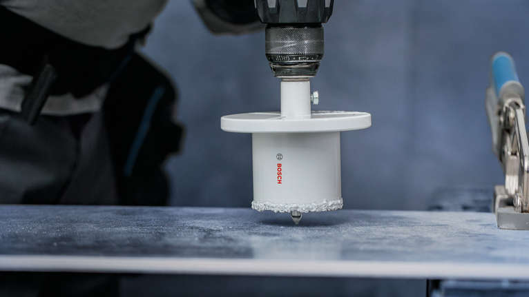 Osoba koja nosi zaštitnu opremu buši veliku rupu u površini pločice.