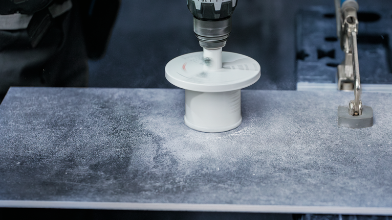 Osoba koja nosi zaštitnu opremu buši veliku rupu u pločici.