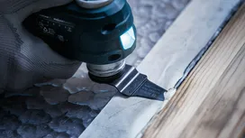 Osoba koja nosi zaštitnu opremu koristi višenamjenski alat za rezanje materijala pored drvenih obloga.