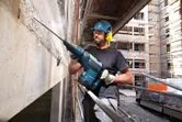 Egy biztonsági felszerelést viselő személy bontókalapácsot használ beton töréséhez egy építkezésen.