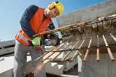 Egy biztonsági felszerelést viselő személy elektromos szerszámmal elvágja a kiálló betonacélt egy építkezésen.