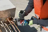 Egy biztonsági felszerelést viselő személy csiszolja a betontömbből kiálló betonacélt.