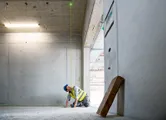 Egy biztonsági felszerelést viselő személy lézeres szintezővel igazítja a pontokat a padlón.
