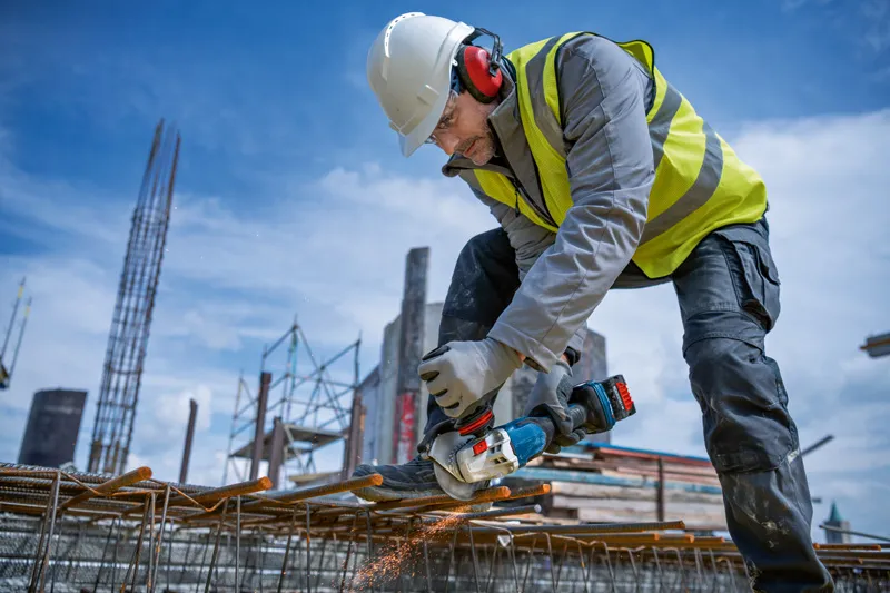 Egy védőfelszerelést viselő személy akkus sarokcsiszolóval csiszolja a betonacélt.