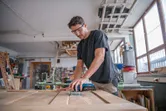 Egy biztonsági felszerelést viselő személy elektromos fűrészt használ fa vágásához egy műhelyben.
