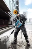 Egy biztonsági felszerelést viselő személy bontja a betont egy építkezésen egy törőgéppel.