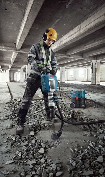 Egy biztonsági felszerelést viselő személy bontja a betonpadlót egy törőgéppel.