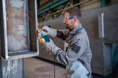 Egy védőfelszerelést viselő személy sarokcsiszolóval fémet csiszol, ami szikrákat ejt.