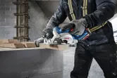 Egy biztonsági felszerelést viselő személy körfűrésszel vág fát egy építkezésen.