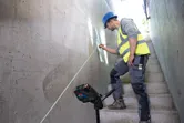 Egy biztonsági felszerelést viselő személy lézeres szintezővel jelöli meg a falat a lépcsőn.