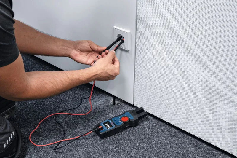 Egy személy villás mérőeszközzel méri a feszültséget egy elektromos aljzatban.