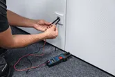 Egy személy villás mérőeszközzel méri a feszültséget egy elektromos aljzatban.