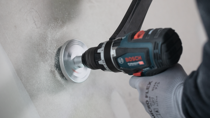 Egy biztonsági felszerelést viselő személy lyukat fúr egy fehér falba.