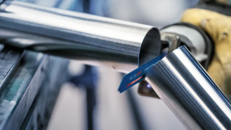 Biztonsági felszerelést viselő személy fémcsövet vág egy dugattyús fűrésszel.