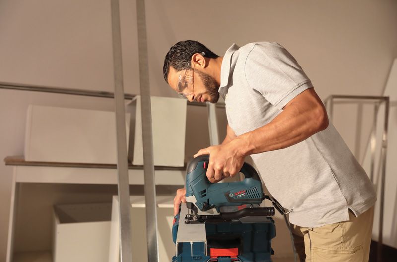 אדם שלובש ציוד בטיחות חותך מתכת בעזרת פאזל על שולחן עבודה.