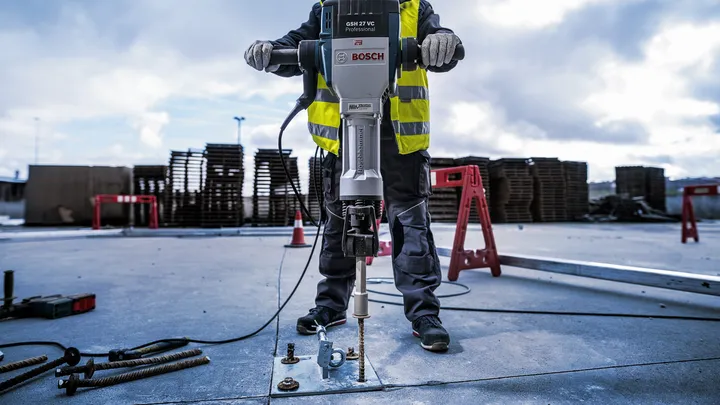 אדם העונד ציוד בטיחות משתמש בפטיש הריסה כדי לשבור בטון בחוץ.