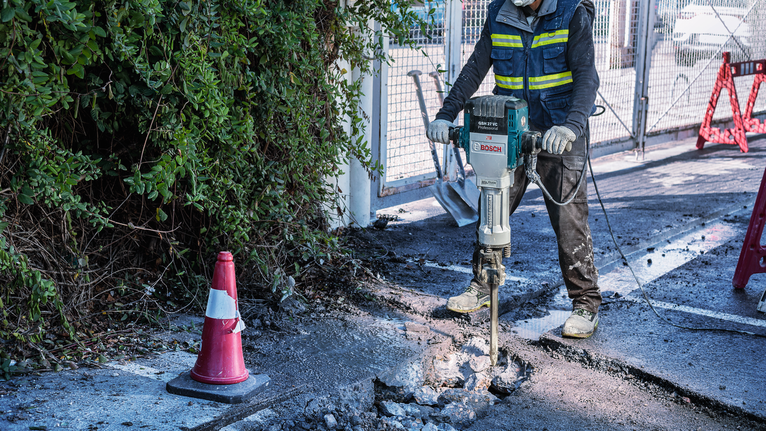 אדם שלובש ציוד בטיחות שובר בטון בעזרת כלי הריסה.