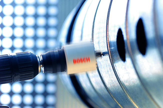 Hole saw attachment drilling into a metal pipe in an industrial setting.