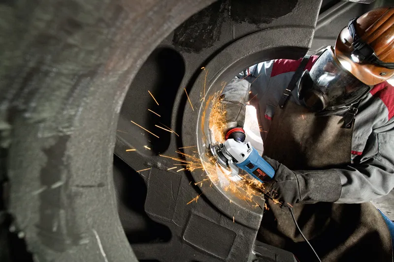 A person wearing safety equipment grinds metal inside a large industrial component.