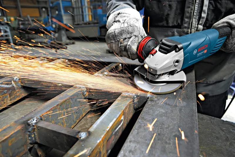 A person wearing safety equipment grinds metal, producing bright sparks.
